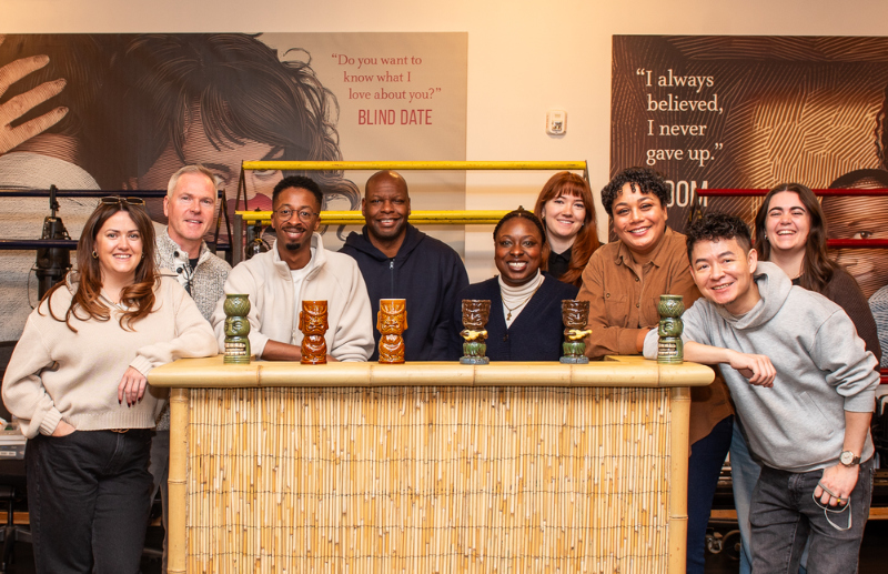 Company of Primary Trust gathers for group photo in the rehearsal hall, with a tiki bar