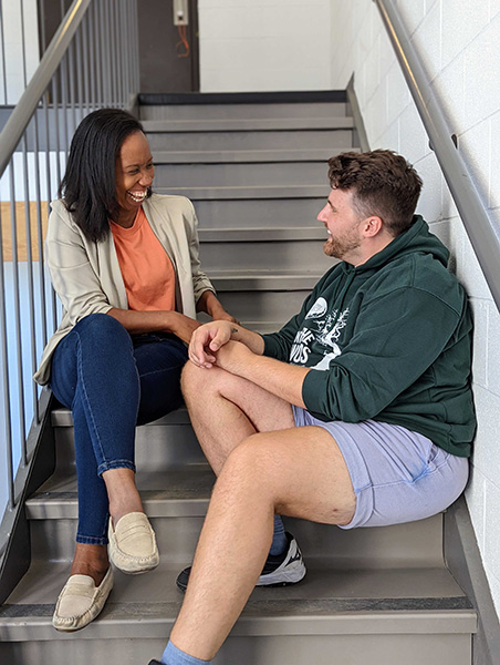 Saccha and Greg laugh together as they sit on a set of stairs.