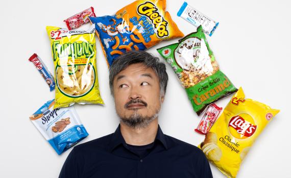 An assortment of convenience store staples - chip bags and chocolate bars - surround Ins Choi on a white background.