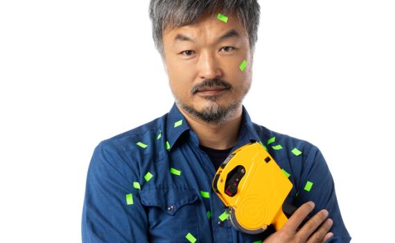 Ins Choi poses against a white backdrop, holding a price labelling gun. His denim shirt peppered with green price tags.