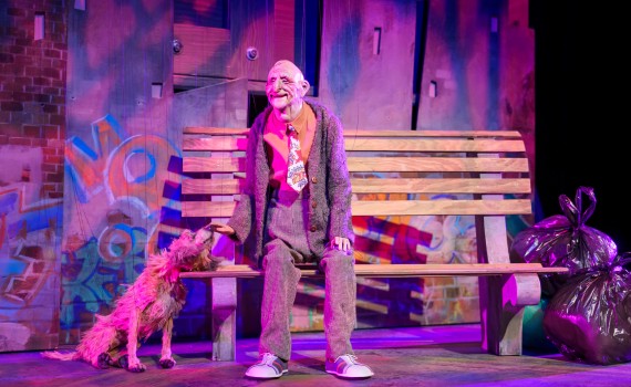 Joe sits on a bench, with his dog Mister beside him. Both are marionettes. 