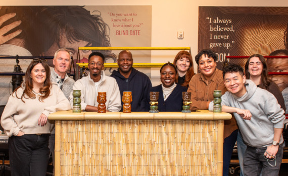 Company of Primary Trust gathers for group photo in the rehearsal hall, with a tiki bar.