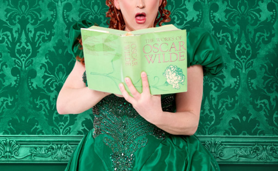 A figure seen in an opulent, emerald green gown, and holding a mint green hardcover Works of Oscar Wilde.