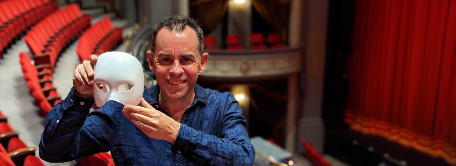 Dennis Garnhum stands in the balcony level of the Spriet Stage at the Grand Theatre, holding a mask from the play Phantom of the Opera.