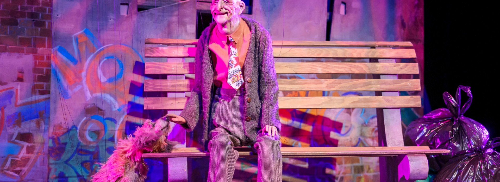 Joe sits on a bench, with his dog Mister beside him. Both are marionettes.