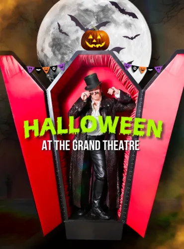 Dracula poses in an upright coffin, surrounded by halloween decor.